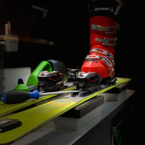 Skiausrüstung mit rotem Schuh und Bindungen auf einem grünen Ski